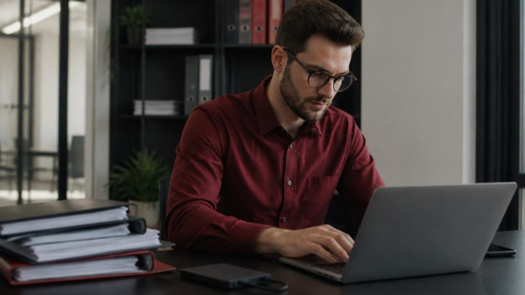 Data analyst cleaning business records on a laptop beside folders of paper files