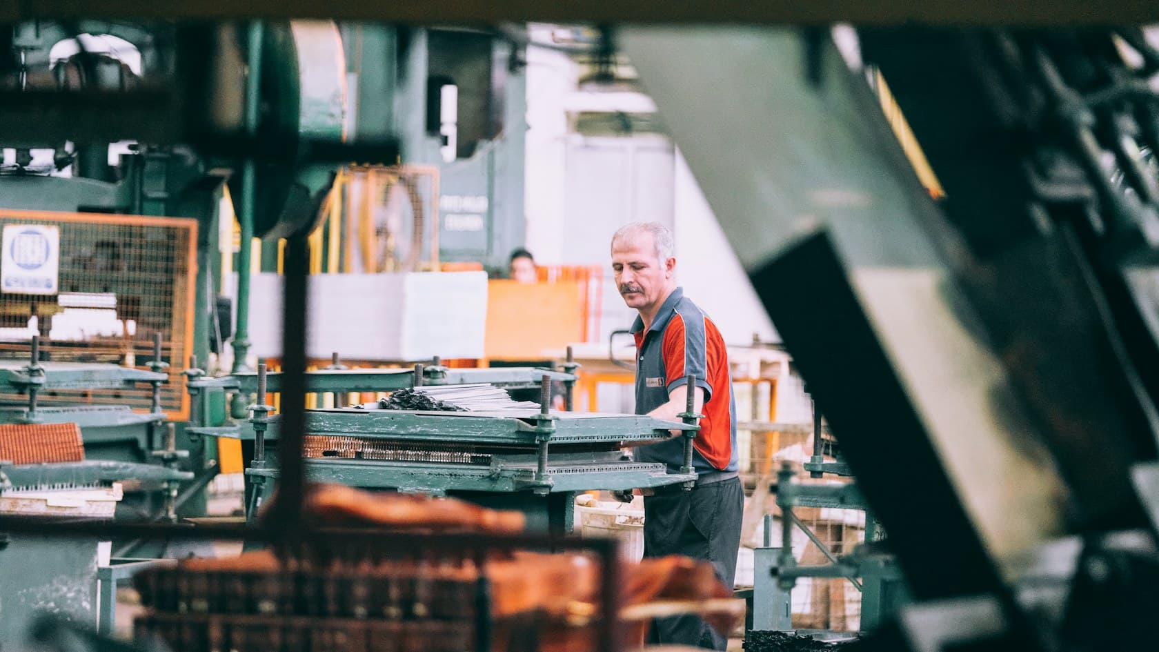 Machine operator in a red and gray shirt working a press on a factory floor